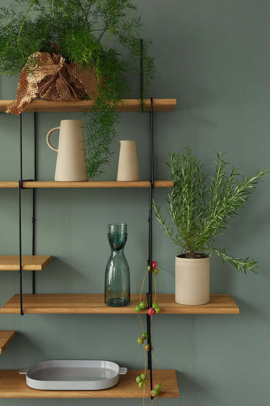 oak shelf on a green wall with plants, vases and decoration in earthy stones on it