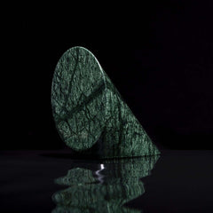 cylinder of green marble cut in a triangle shape on sitting on small black rocks