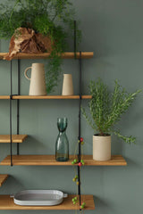 oak shelf on a green wall with plants, vases and decoration in earthy stones on it